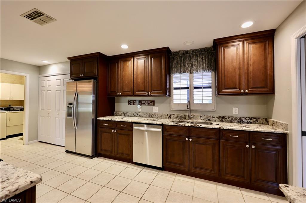 Kitchen featuring stainless steel appliances, light stone countertops, light tile patterned flooring, recessed lighting, and dark wood finish cabinetry