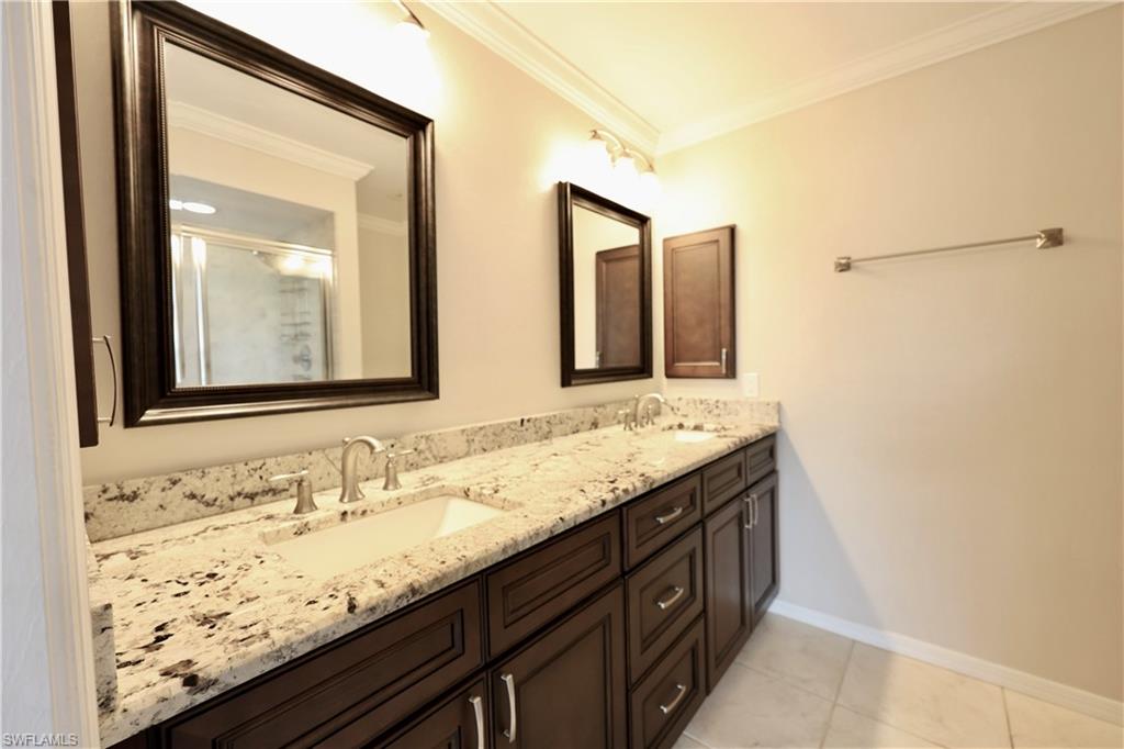 Bathroom featuring double vanity, crown molding, a shower stall, and light tile patterned floors