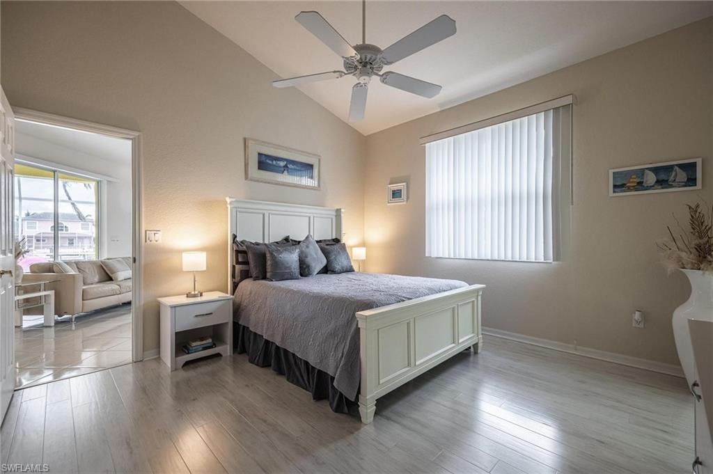 Bedroom with lofted ceiling, light wood-style floors, multiple windows, and a ceiling fan