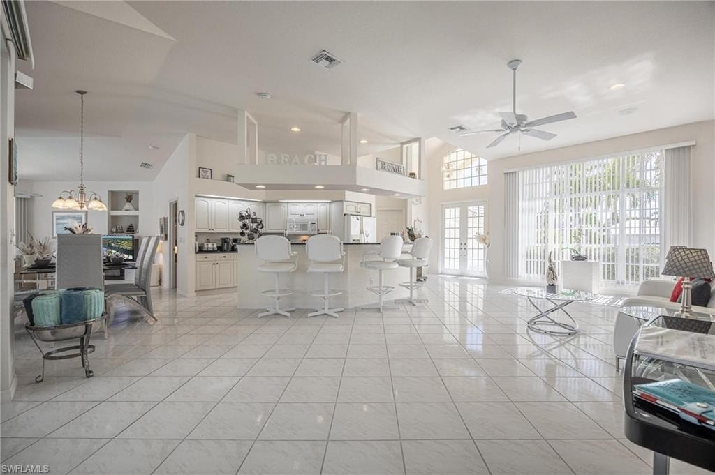 Living area featuring a high ceiling, light tile patterned flooring, french doors, a ceiling fan, and hanging lights