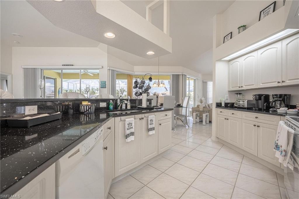 Kitchen featuring white appliances, dark stone counters, recessed lighting, a high ceiling, and white cabinetry