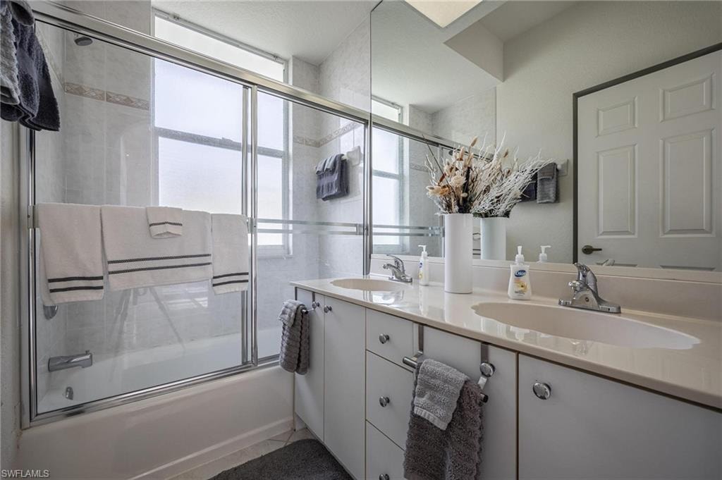 Bathroom featuring combined bath / shower with glass door and double vanity