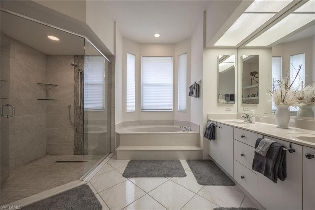 Full bathroom with double vanity, a stall shower, a bath, light tile patterned floors, and recessed lighting
