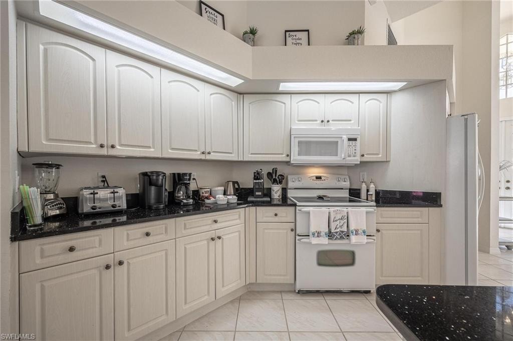 Kitchen featuring white appliances, dark stone countertops, white cabinets, a high ceiling, and light tile patterned flooring
