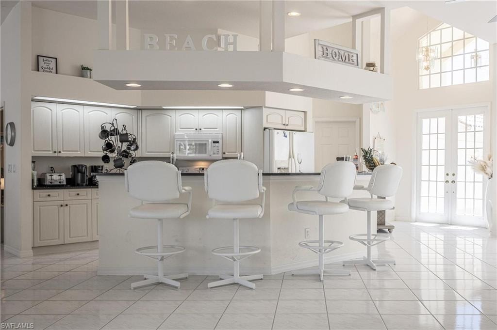 Kitchen with french doors, dark countertops, white appliances, a breakfast bar area, and lofted ceiling