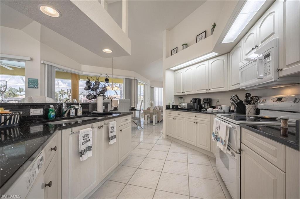 Kitchen featuring white appliances, dark stone counters, lofted ceiling, light tile patterned floors, and recessed lighting