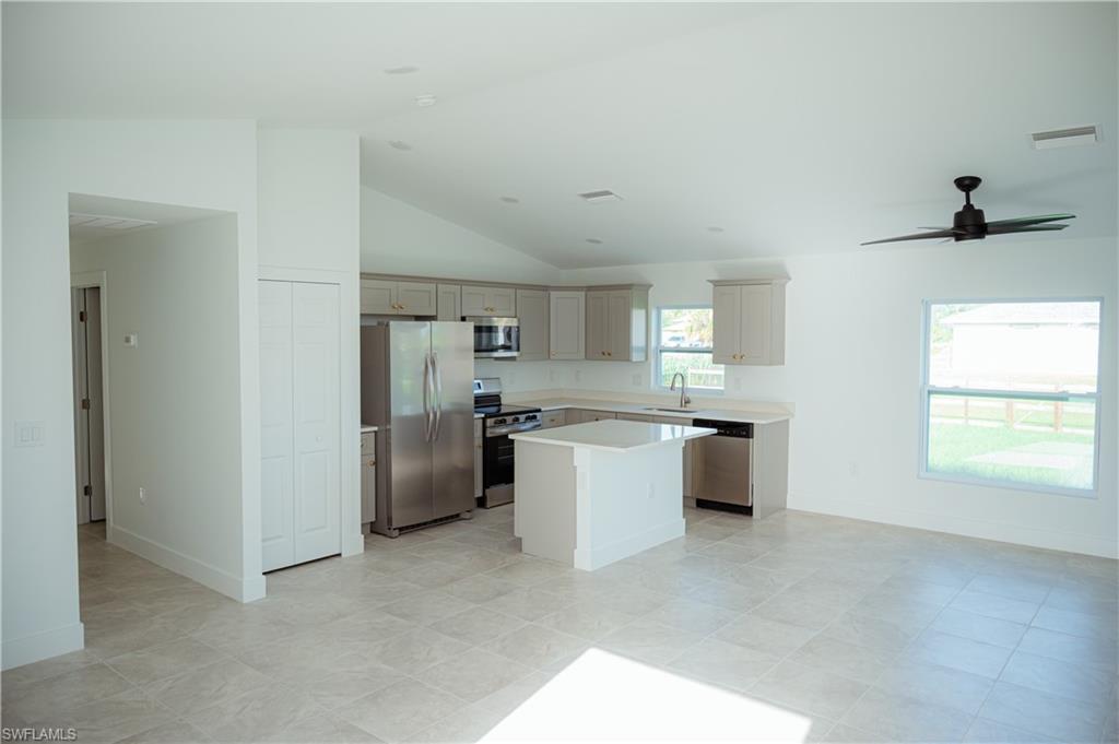 Open-concept kitchen and living area featuring vaulted ceilings, light-toned tile flooring, and a modern ceiling fan