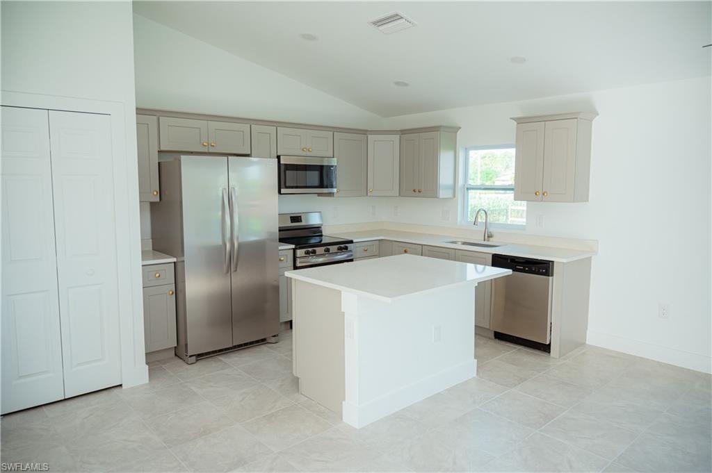 Open-concept kitchen featuring shaker-style cabinetry, a central island with a solid surface countertop, stainless steel appliances, and large format tile flooring