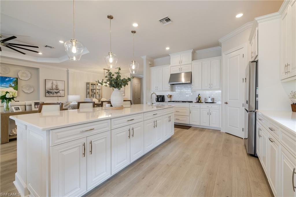Kitchen featuring ornamental molding, white cabinetry, pendant lighting, a large island with sink, and freestanding refrigerator
