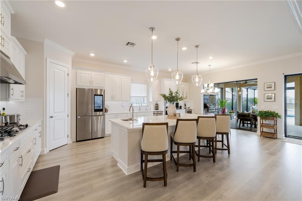 Kitchen featuring an island with sink, a kitchen breakfast bar, stainless steel appliances, white cabinets, and light wood-style flooring
