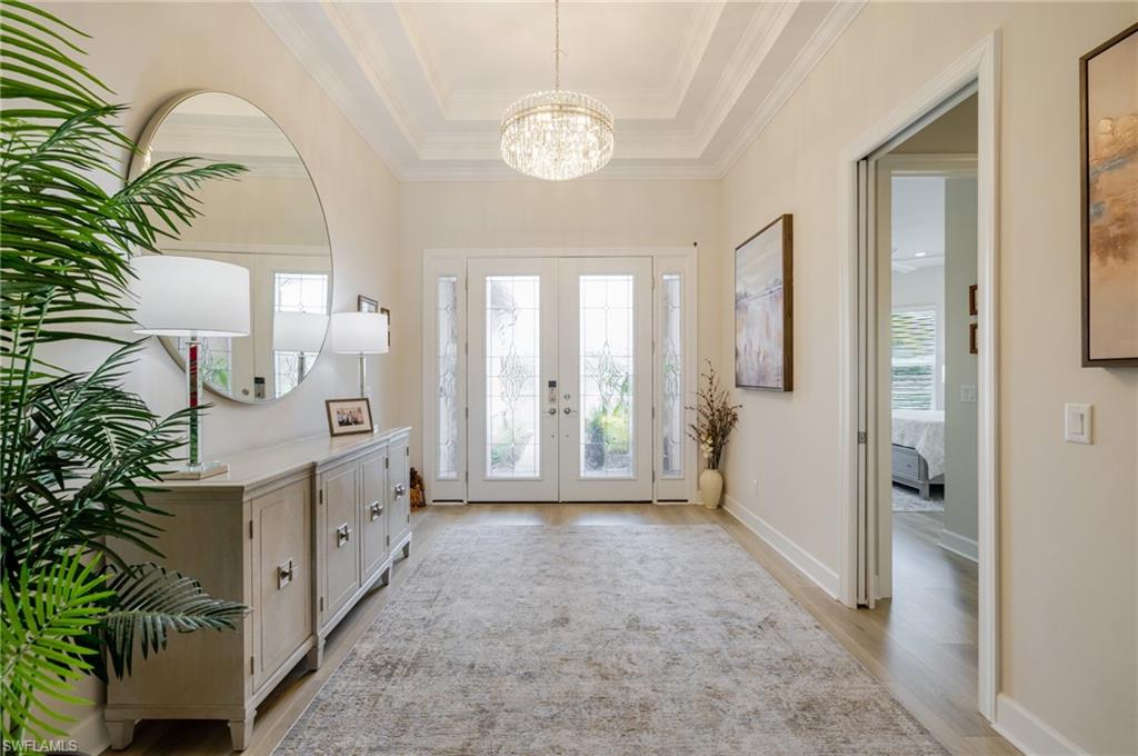 Foyer entrance with a tray ceiling, a chandelier, french doors, and light wood-style flooring