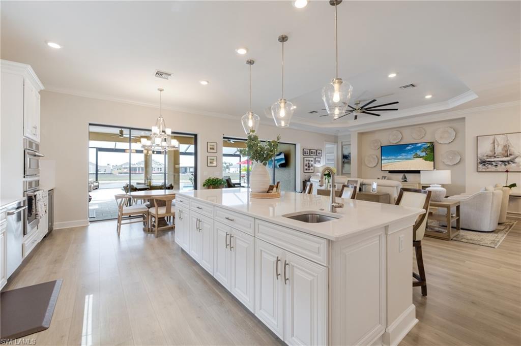 Kitchen featuring white cabinetry, a breakfast bar, light stone counters, crown molding, and a kitchen island with sink