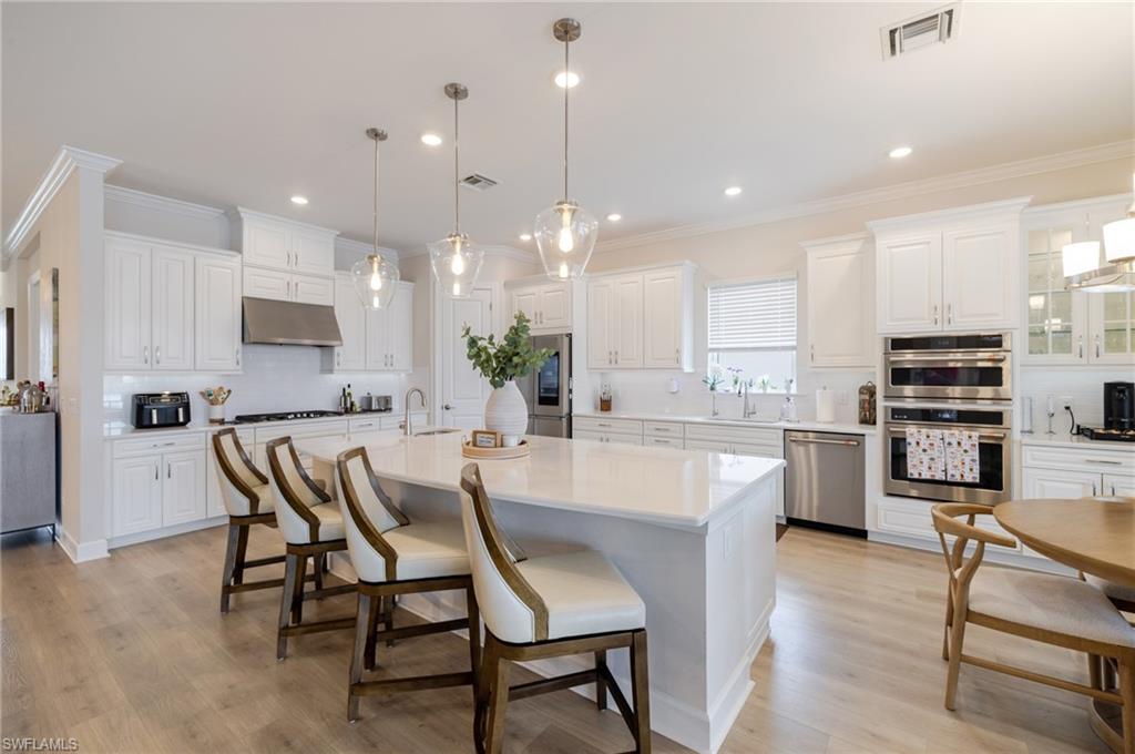 Kitchen featuring decorative backsplash, white cabinetry, a breakfast bar area, a large island with sink, and ornamental molding