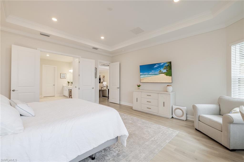 Bedroom with light wood-style floors, ornamental molding, recessed lighting, a tray ceiling, and connected bathroom