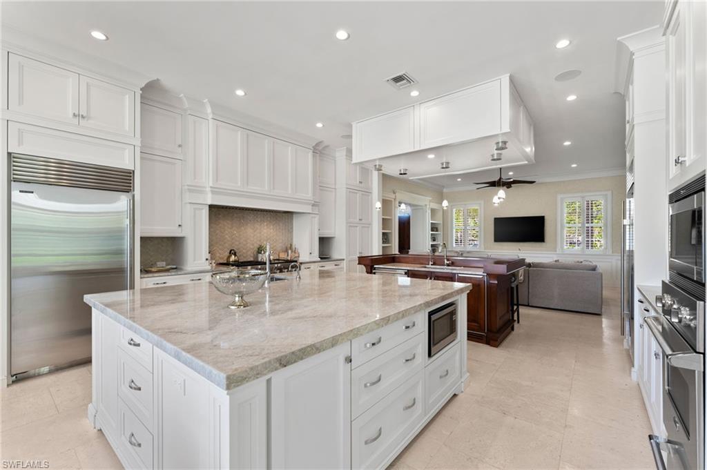 Kitchen with built in appliances, ornamental molding, open floor plan, visible vents, and a large island with sink