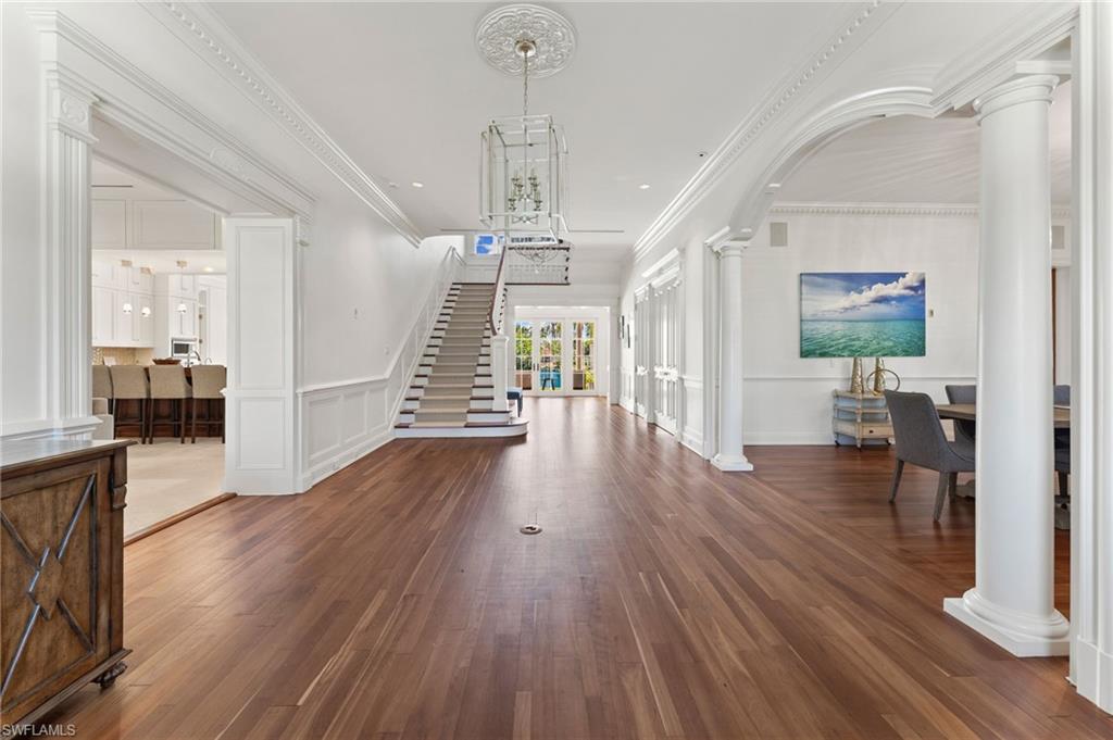 Entryway with a decorative wall, ornate columns, ornamental molding, wood finished floors, and stairs