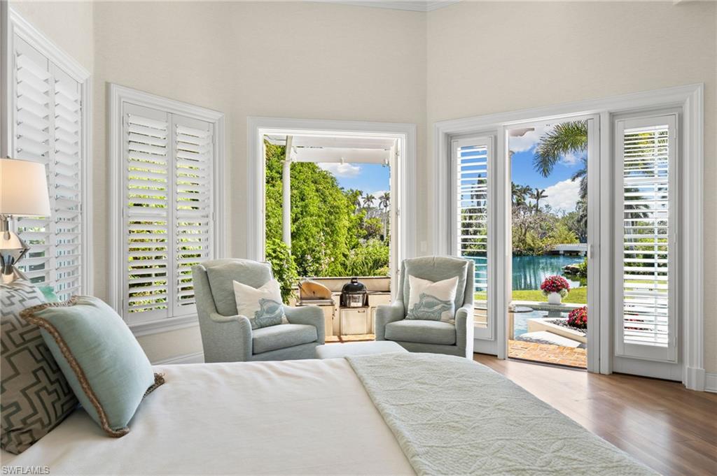 Bedroom featuring a towering ceiling, access to outside, baseboards, a water view, and wood finished floors
