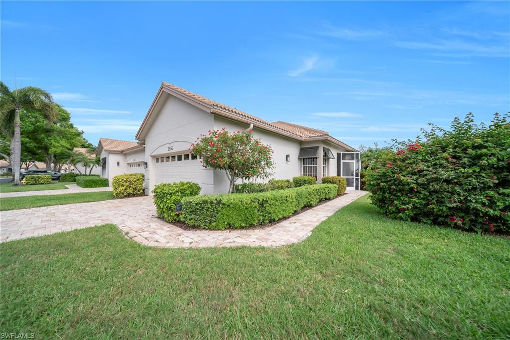 View of side of home featuring stucco siding, a yard, a garage, a tile roof, and driveway