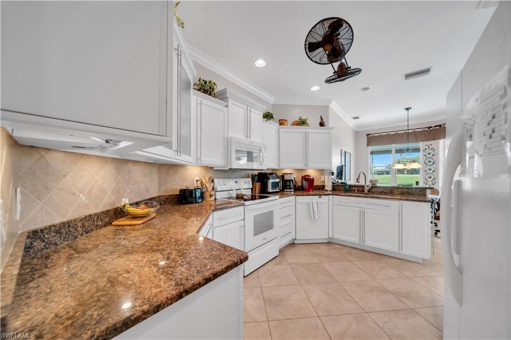 Kitchen featuring a peninsula, white appliances, dark stone counters, white cabinetry, and ornamental molding