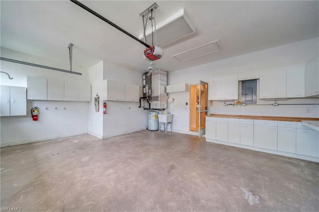 Garage featuring water heater, heating unit, electric panel, and a garage door opener