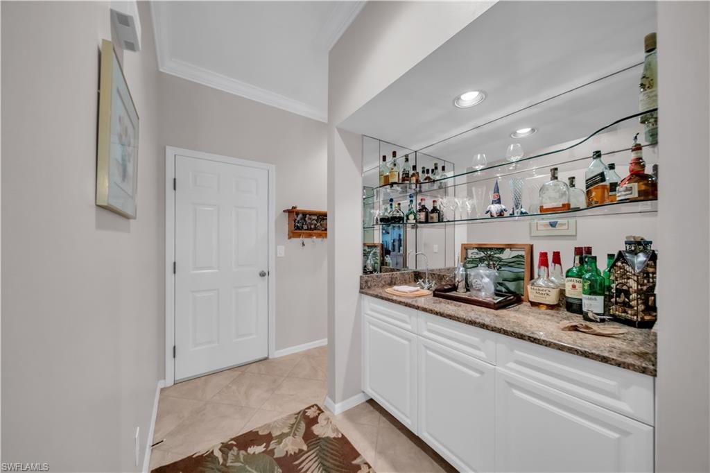 Indoor wet bar with dark stone countertops, white cabinets, crown molding, open shelves, and light tile patterned flooring