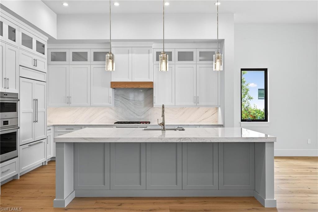 Kitchen featuring glass fronted cabinets, light counters, decorative light fixtures, and wood finished floors