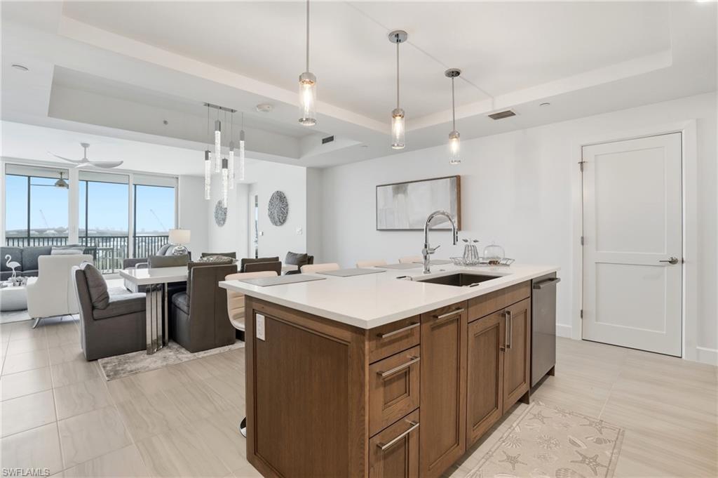 Kitchen featuring a tray ceiling, pendant lighting, open floor plan, and a center island with sink - Virtually Edited Image