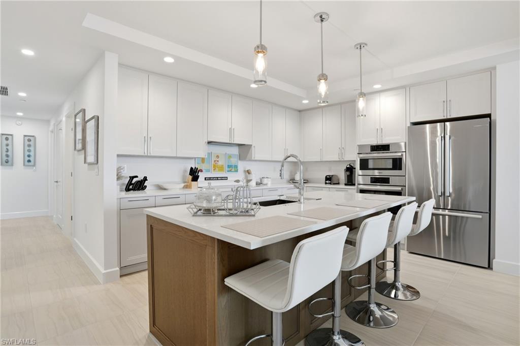 Kitchen featuring stainless steel appliances, white cabinetry, a kitchen breakfast bar, and recessed lighting - Virtually Edited Image