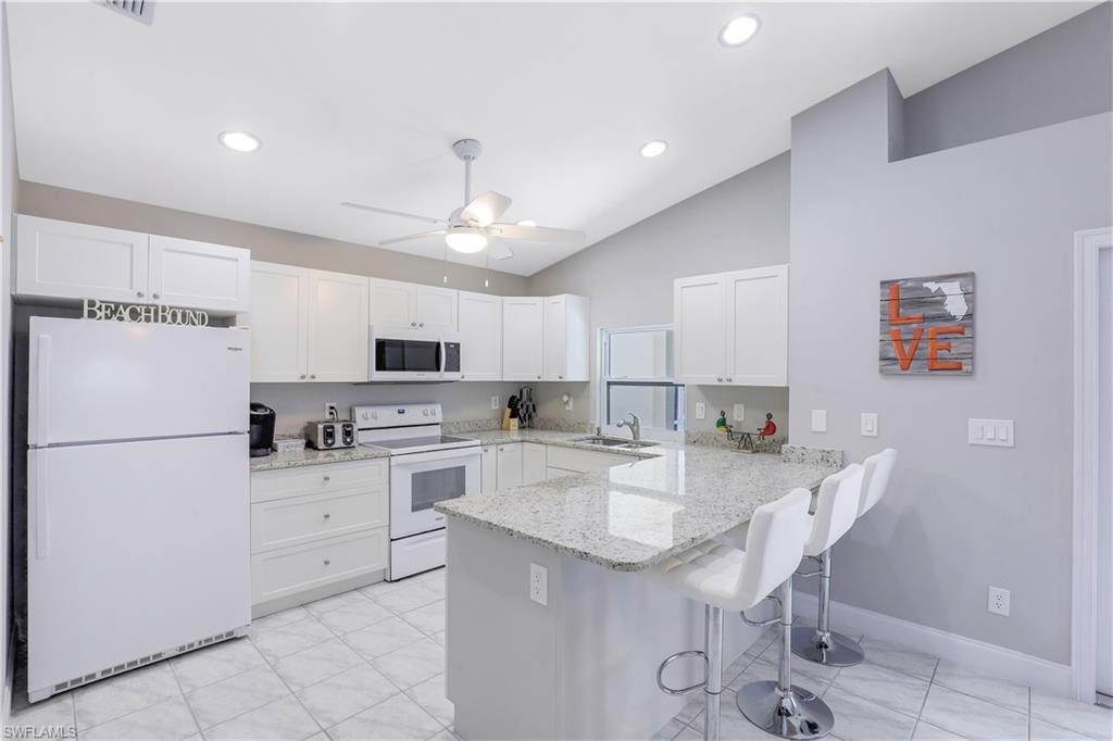 Kitchen featuring white appliances, light stone countertops, white cabinetry, a peninsula, and a kitchen bar