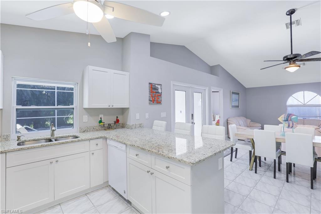 Kitchen with ceiling fan, light stone counters, open floor plan, a peninsula, and lofted ceiling