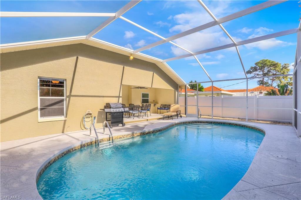 View of swimming pool featuring glass enclosure, a sunroom, a grill, and patio surround