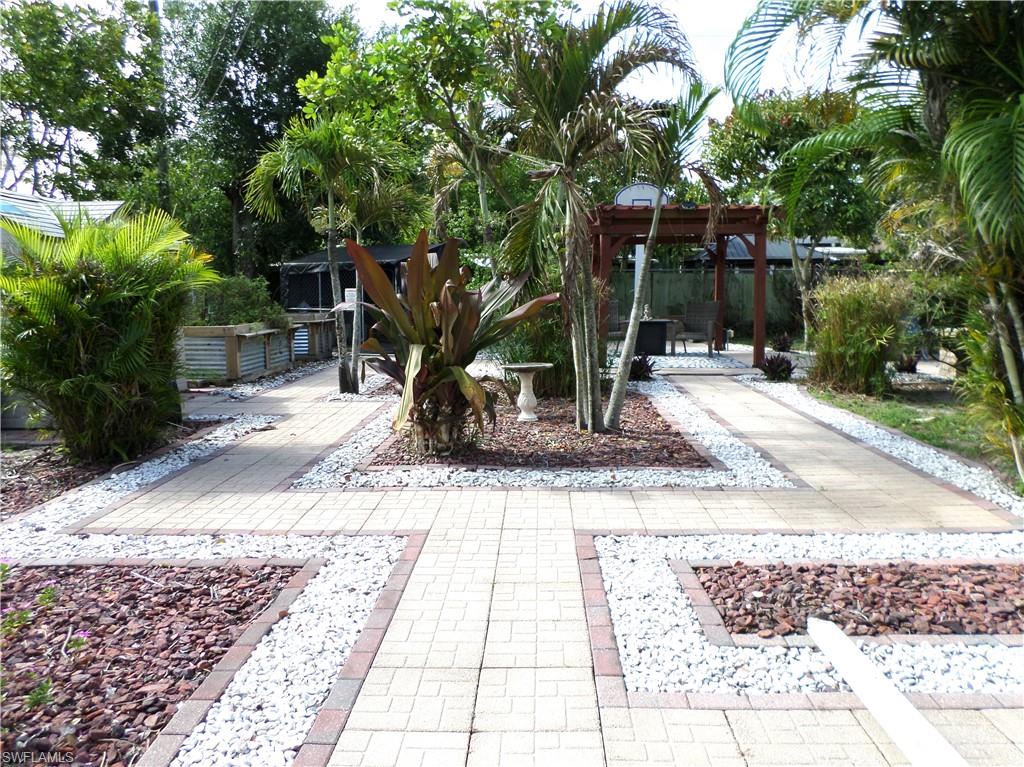 Over Size Fenced Courtyard Type Back Yard, Paved & Some Grass Area, Palm Trees & A Fruit Tree & Different Plants.