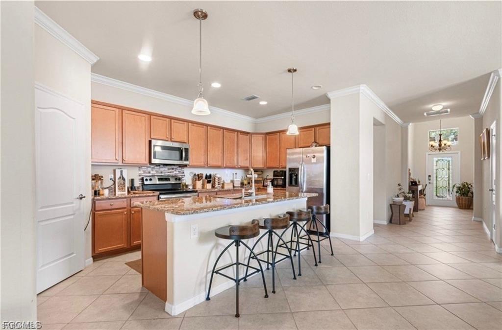 Kitchen featuring a kitchen bar, stainless steel appliances, an island with sink, light stone counters, and ornamental molding