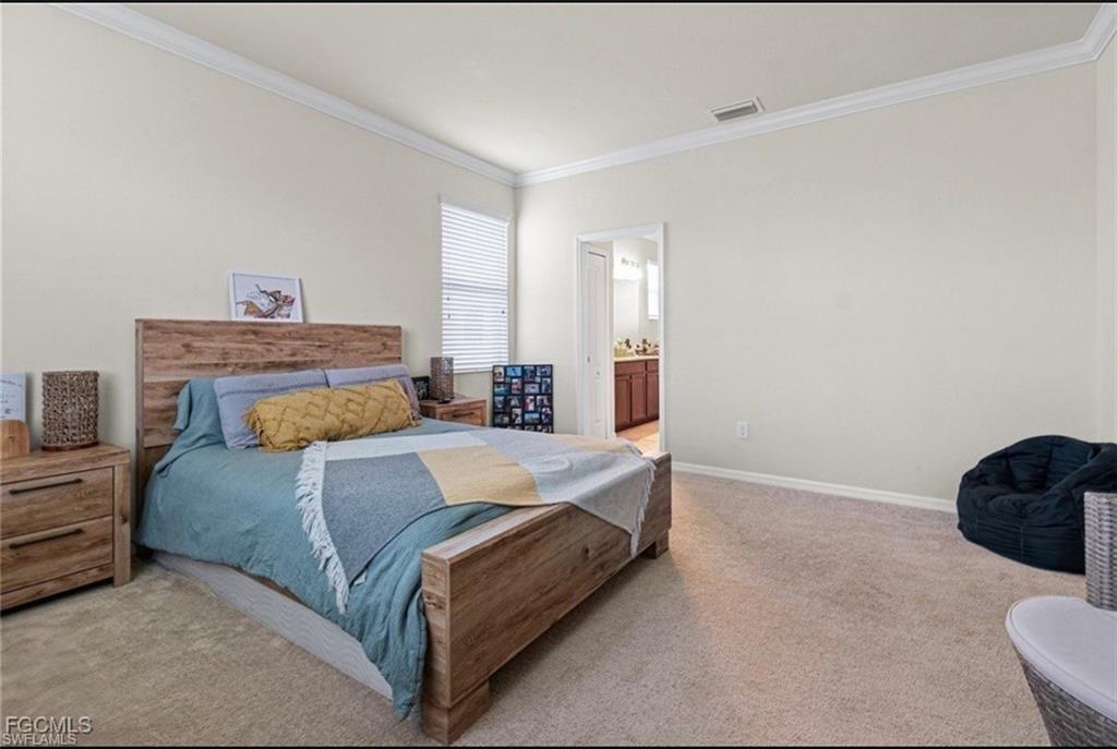 Bedroom with light colored carpet, ornamental molding, and ensuite bath