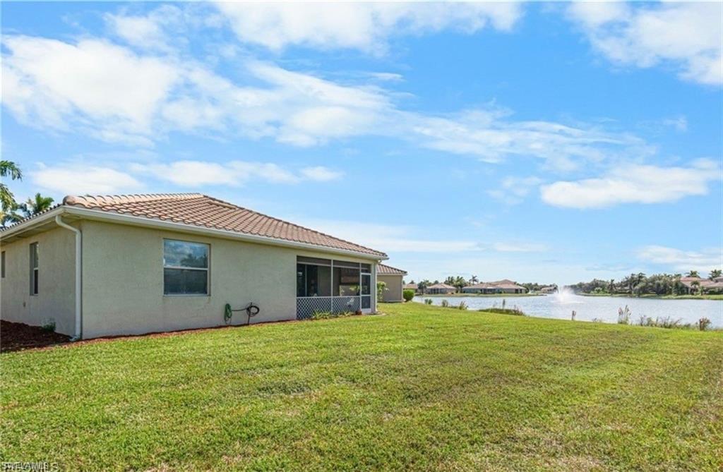 Back of property featuring a sunroom, a yard, stucco siding, a water view, and a tiled roof