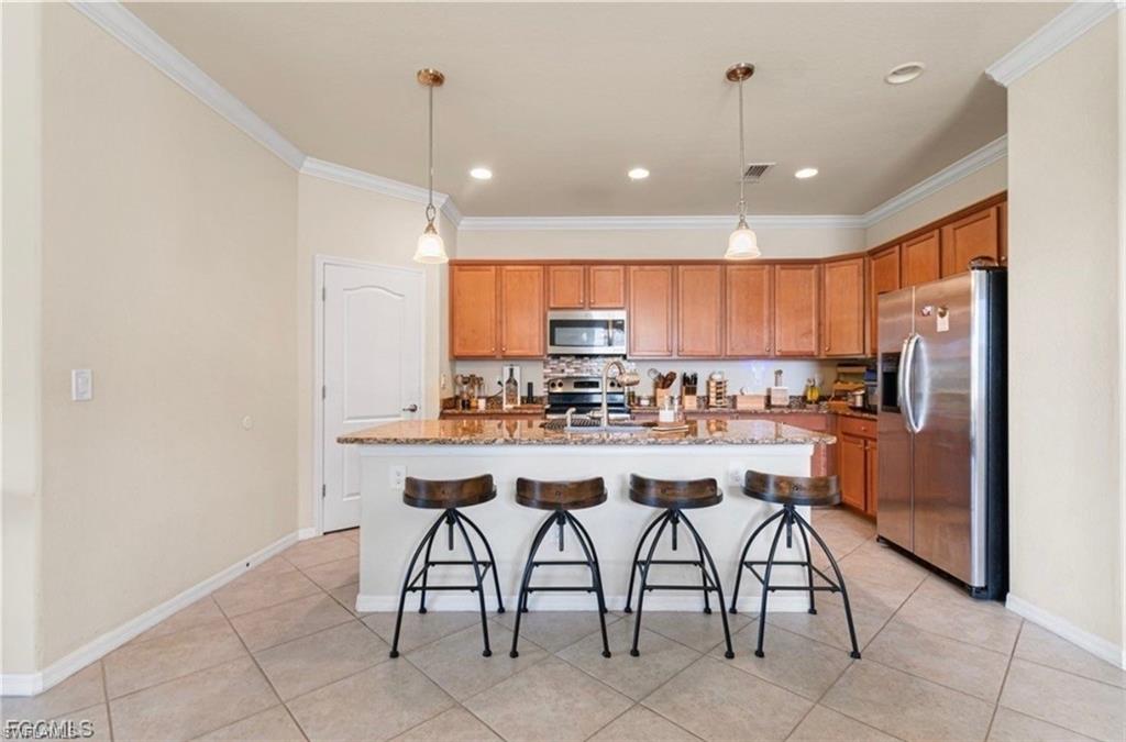 Kitchen featuring stainless steel appliances, light stone countertops, a kitchen island with sink, hanging light fixtures, and ornamental molding