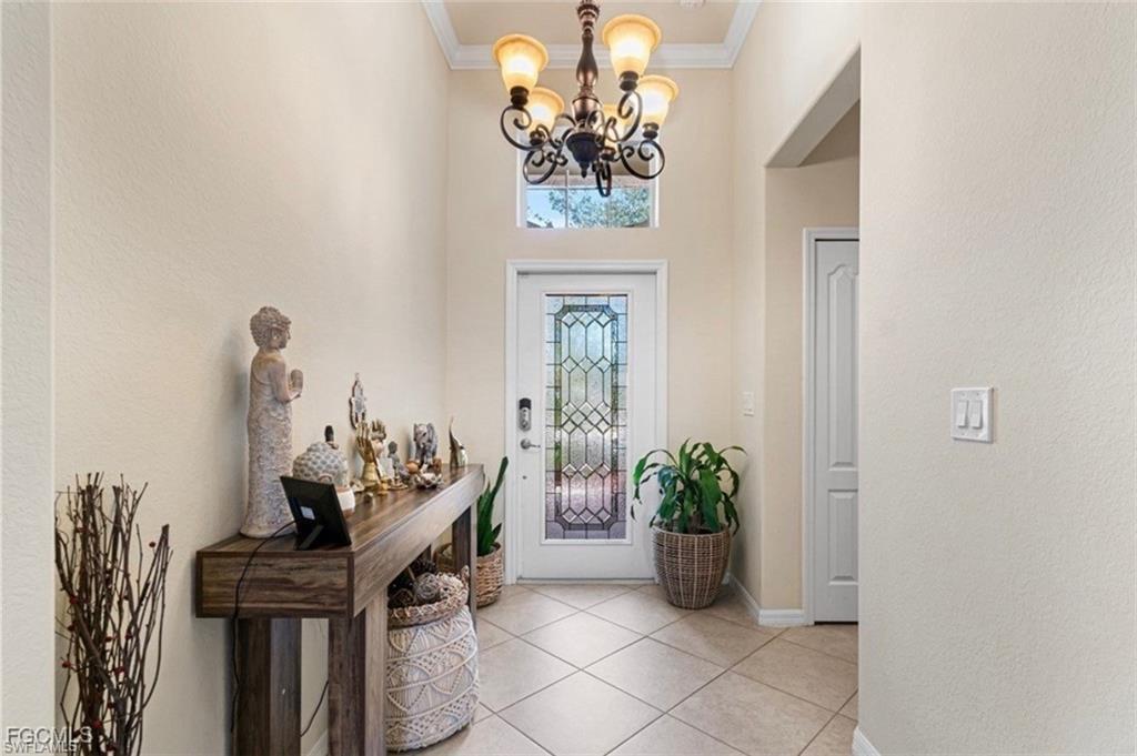 Foyer featuring a chandelier, crown molding, a textured wall, a high ceiling, and light tile patterned floors