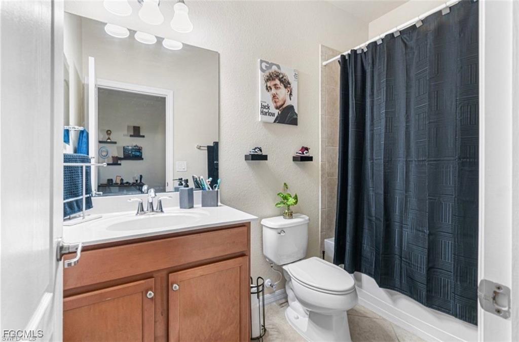 Full bathroom featuring a textured wall, vanity, shower / bath combination with curtain, and light tile patterned floors