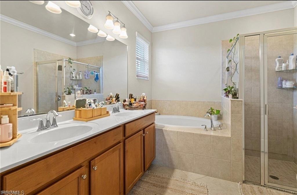 Full bath with crown molding, double vanity, a stall shower, a bath, and light tile patterned flooring