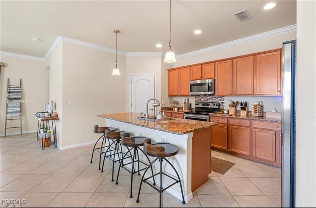 Kitchen with dark stone countertops, a breakfast bar, stainless steel appliances, an island with sink, and hanging light fixtures