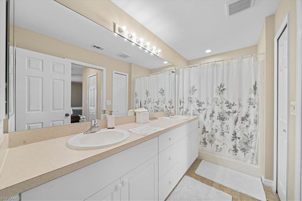 Full bath with double vanity, curtained shower, light tile patterned floors, and a closet