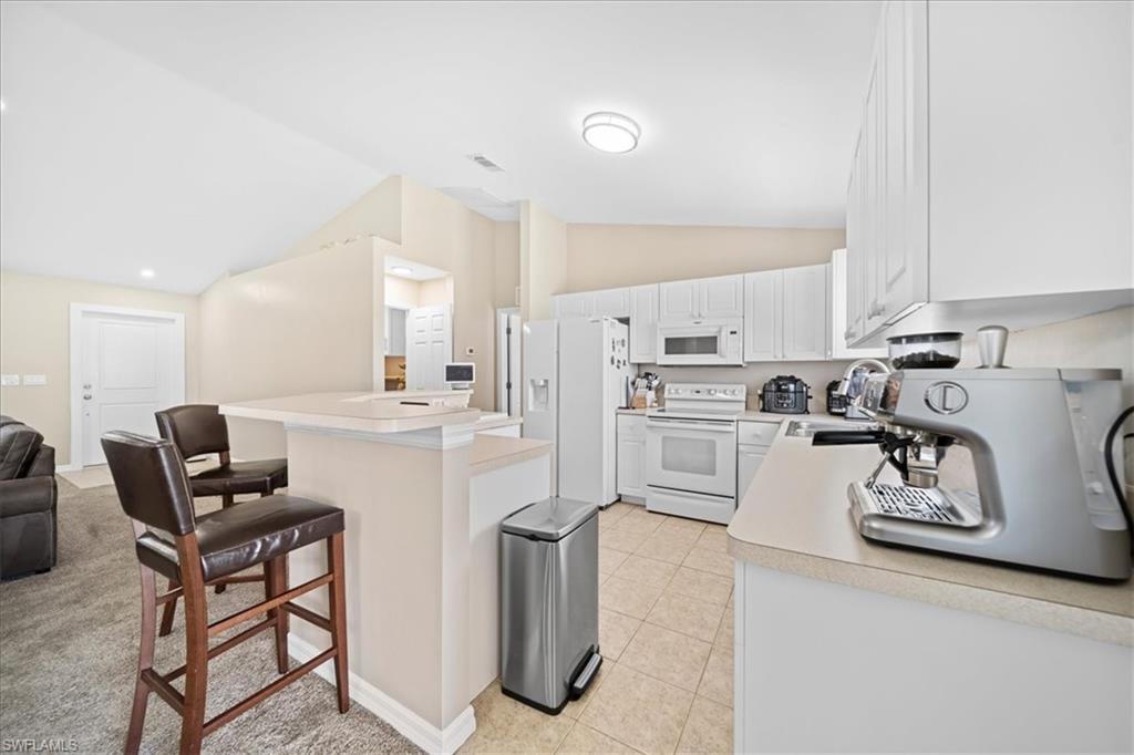Kitchen with vaulted ceiling, white appliances, light countertops, a breakfast bar, and white cabinetry