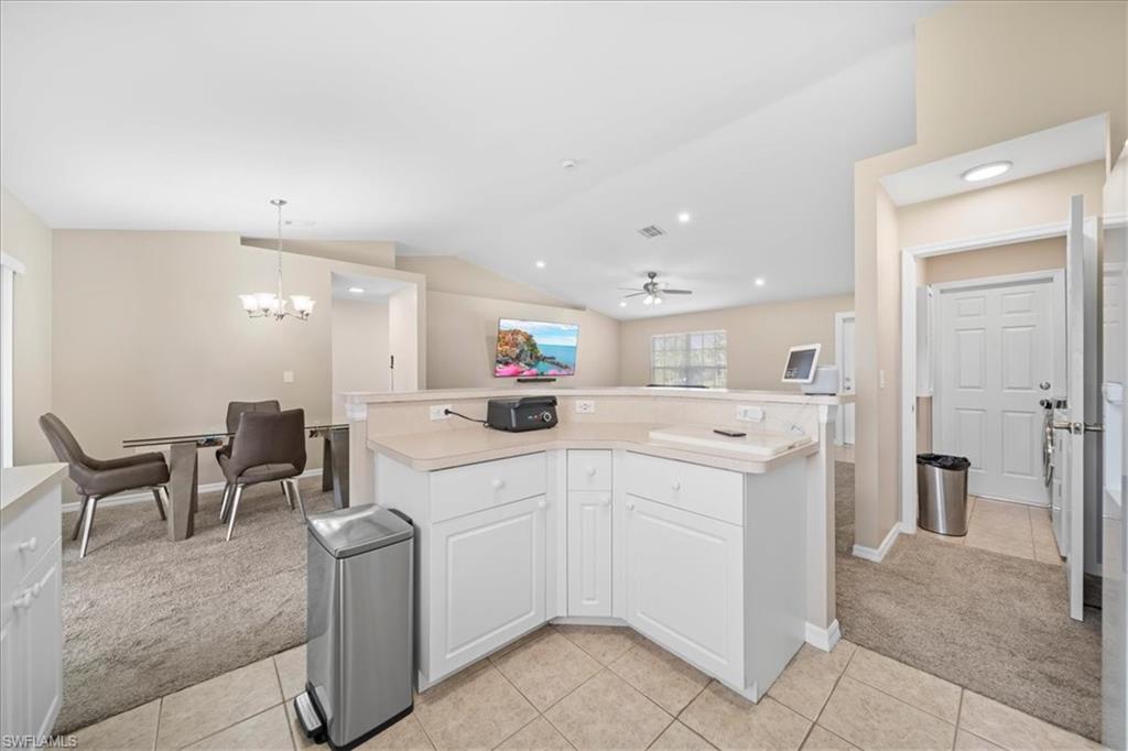 Kitchen featuring light carpet, lofted ceiling, a kitchen island, white cabinetry, and a ceiling fan