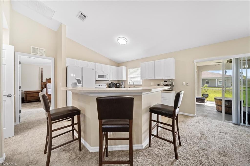 Kitchen featuring light carpet, white cabinets, a breakfast bar area, light countertops, and white appliances