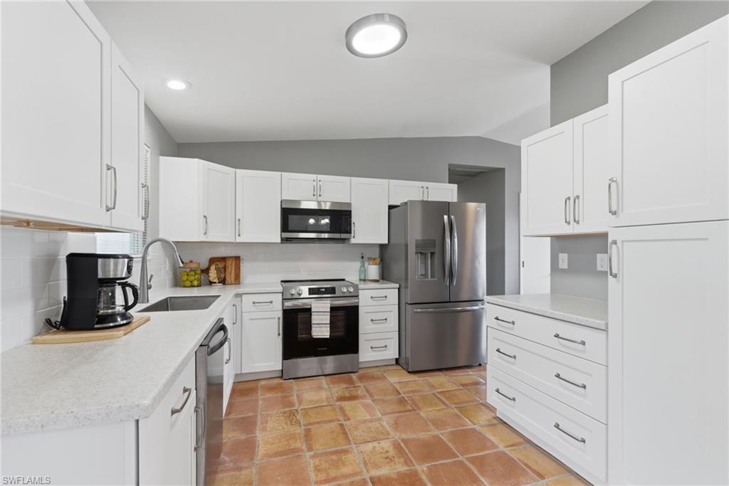NEW Kitchen with stainless steel appliances, lofted ceiling, white cabinetry, tasteful backsplash, and light stone counters