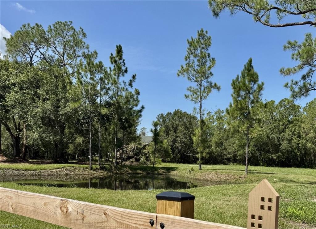 Expansive outdoor space featuring a body of water, mature trees, and a wooden fence