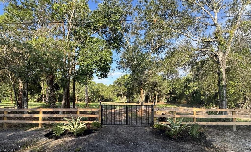 Black metal double gate entry with a wood-plank fence