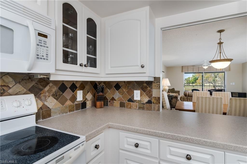 Kitchen featuring decorative backsplash, white appliances, and glass insert cabinets