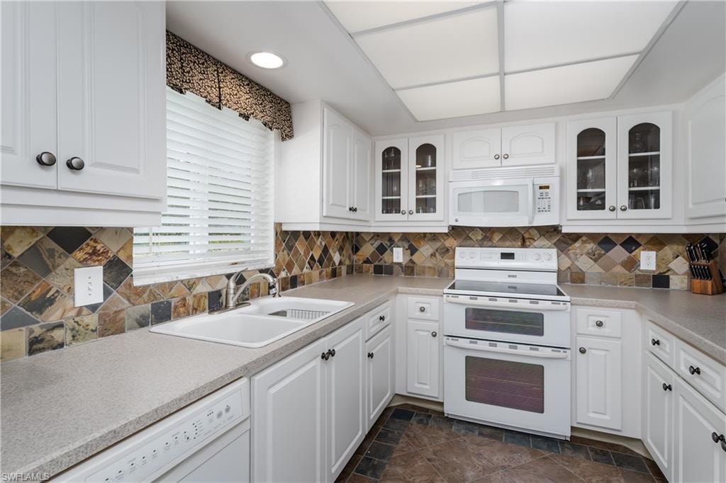 Kitchen with white cabinetry, a sink, white appliances, and glass insert cabinets