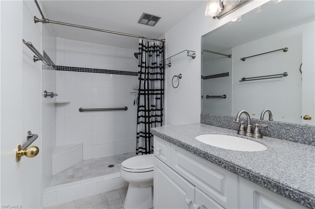Bathroom featuring a tile shower, toilet, vanity, and visible vents